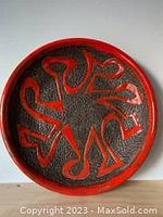 Top view of large round ceramic plate showing textured black surface with bold red glaze abstract pattern