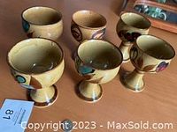 Set of six stoneware goblets with pedestal bases, varying hand-painted mid-century abstract designs in muted colors, shown on wooden table.