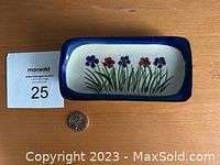 Top view of small rectangular pottery dish with hand painted floral design and blue border, alongside a coin for scale.