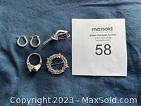 Five sterling silver jewelry pieces on dark fabric: two brooches, one pair of hoop earrings, one ring, beside a MaxSold numbered paper.