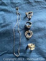 Full photo of sterling silver chain and four rings arrayed on blue cloth