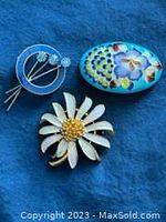 Three colorful enamel brooches: white daisy, oval floral, and circular abstract designs