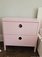 Front view of pink 2-drawer chest IKEA BUSUNGE with circular cut-out handles.