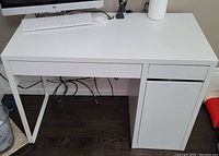 Front view of white desk showing tabletop, central drawer and right-side cabinet door closed