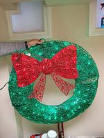 Wreath held upright showing green wired structure with integrated green lights and a large red wired bow attached.