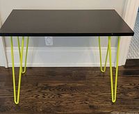 Side view of rectangular black side table with bright green hairpin legs on wooden floor.