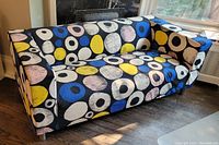 Full front view of IKEA Klippan sofa with colorful circular patterned fabric cover, showing overall shape and condition with some wear.