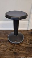 Black ECR 4 Kids stool shown upright on wooden floor with rounded octagonal seat and round base.