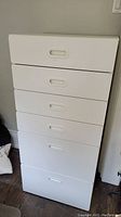 Front view of white IKEA FRITIDS cabinet with 6 drawers, stacked vertically against a wall on wooden floor.
