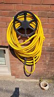 Full view of yellow Stanley Fatmax water hose coiled on a black plastic hose reel mounted on a brick wall.