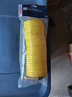 New yellow recoil air hose coiled in original plastic packaging, showing hose and fittings.