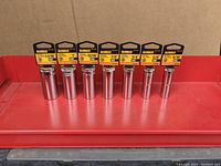 Front view of all 7 DeWalt deep sockets arranged side by side on red surface, showing packaging labels clearly.