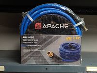 Front view of coiled Apache PVC air hose labeled with 3/8 inch x 25 feet, 300 PSI, XtremeFlex technology, showing product packaging and brass fittings.