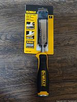 Dewalt 1-inch side strike chisel front view in packaging on wood background showing branding, blade, and handle.