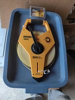 Full view of new Johnson Big J Series fiberglass reel with 300ft yellow tape in a gray plastic tray, showing the complete reel with crank handle and attached tape hook.