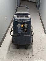 Front view of the upright MasterCraft air compressor showing handle, wheels, and control panel with gauges and pressure regulator knob.