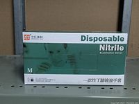 Box of disposable nitrile gloves size medium on a metal shelf, showing front and top with branding and product information.
