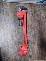 Photo showing the full length of the red Task pipe wrench placed on a wooden surface.