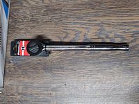 Full view of new Powerbuilt 1/2 inch drive ratchet on wooden surface showing the full length and chrome finish.