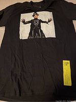 Front view of black T-shirt with graphic print of Boy George in hat and arms outstretched
