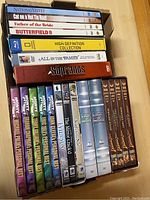 Stack of DVD and Blu-ray box sets including various movies and TV series stacked on top of each other in a cardboard box.