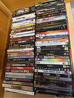Photo showing a stack of about 50 DVD movies in cases arranged on a wooden surface with various titles visible.