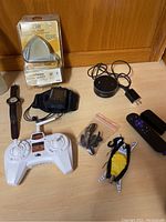 Overview of all lot items on light wood surface showing watch, drone controller, earphones, Roku remote, toy drone, and packaging for card reader.