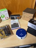 Overview of all items in lot including boxed EVGA PD02 zero client, OontZ speaker, Coby CD player, power strip, and others on wooden surface