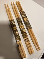 Three pairs of Hard Rock Cafe branded wooden drum sticks bundled with paper bands on white surface.