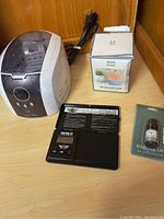 Jewelry ultrasonic cleaner, digital scale, aroma diffuser box, and essential oil bottle arranged on wooden surface.