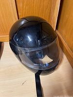Front and top view of a glossy black full-face motorcycle helmet showing clear visor and chin strap.