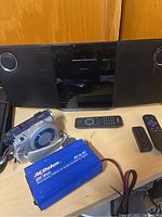 Philips dock station, Sony Handycam, power inverter, Roku sticks with remotes, and Apple adapter on wooden surface