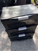 Front view of stacked black plastic storage drawers with three drawers featuring silver handles and textured tops