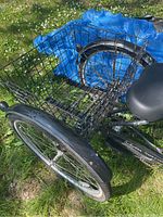 View of the rear wheel with large black wire mesh cargo basket attached over two rear wheels, black cushioned seat visible.