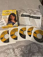 Five Spanish V2.0 language learning CDs, instruction sheet, and original box on a cloth surface.