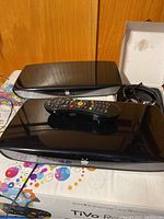 Two TiVo Roamio DVR units stacked with one remote control on top, placed on a colorful surface.