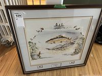 Full view of the framed art print showing a large trout, fishermen on boat and shore, surrounded by fly fishing fly illustrations.