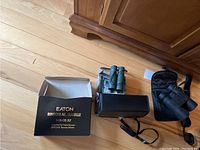 All three pairs of binoculars arranged on the floor with Eaton box and leather case visible.