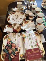 Overview of the lot showing Royal Albert Country Rose china items, decorative clock plate, mugs, serving pieces, glassware, and linens.