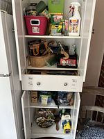 Photo showing inside white cabinet shelves with an assortment of garden supplies including pink container, green kneeling pad, insect sprays, seed packets, and Fiskars tools.