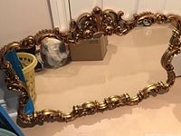 Front view of the gilded ornate mirror showing detailed carved floral and scroll design frame.