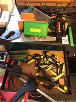 Overall view of mitre boxes, hand saws, punch set green case, and assortment of clamps inside a drawer.