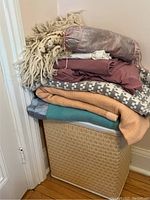 Stack of blankets, sheets and throws on top of a vintage woven hamper.