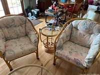 Two matching rattan arm chairs with floral upholstered cushions and a matching rattan end table with glass top seen from above in living room.