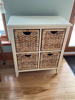 Front view of the wooden storage unit showing four woven wicker basket drawers in a white painted wooden frame.
