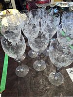 Photo showing multiple large and smaller Stuart Crystal stem glasses with etched floral designs grouped on table.