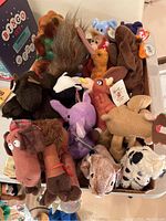 Top view of multiple TY Beanie Babies plush toys and other small stuffed animals in a box, showing variety of animal shapes and colors with visible TY tags.