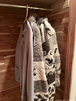 Three sweater coats hanging in a cedar closet, showing lot contents including grey cardigan and patterned sweater coat