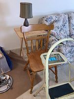 Wooden chair in front of folding wooden TV table and table lamp, with sofa in background