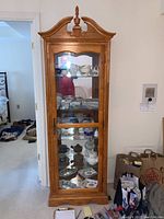 Front view of the full height wooden display cabinet showing decorative crown, glass door and visible shelves with contents inside.